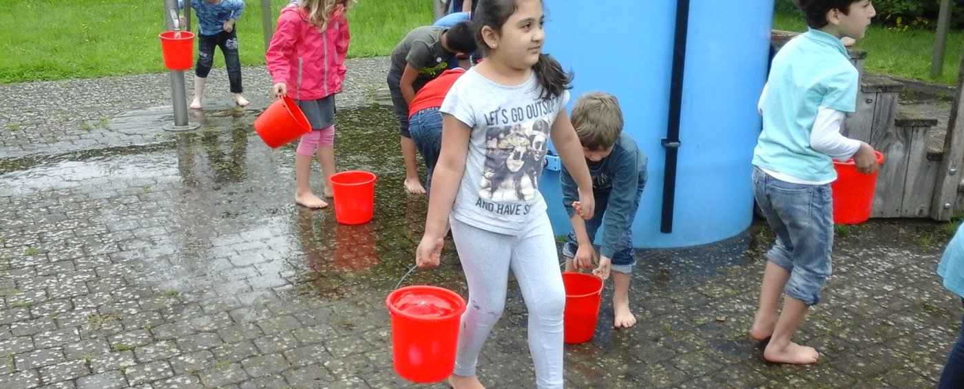 Auf dem Bild sind Kinder zu erkennen, welche einen Eimer mit Wasser tragen
